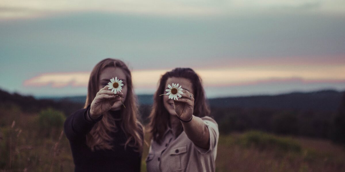 Due ragazze con sullo sfondo un tramonto mostrano due margherite.